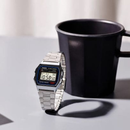 Digital watch next to a black mug on a light surface